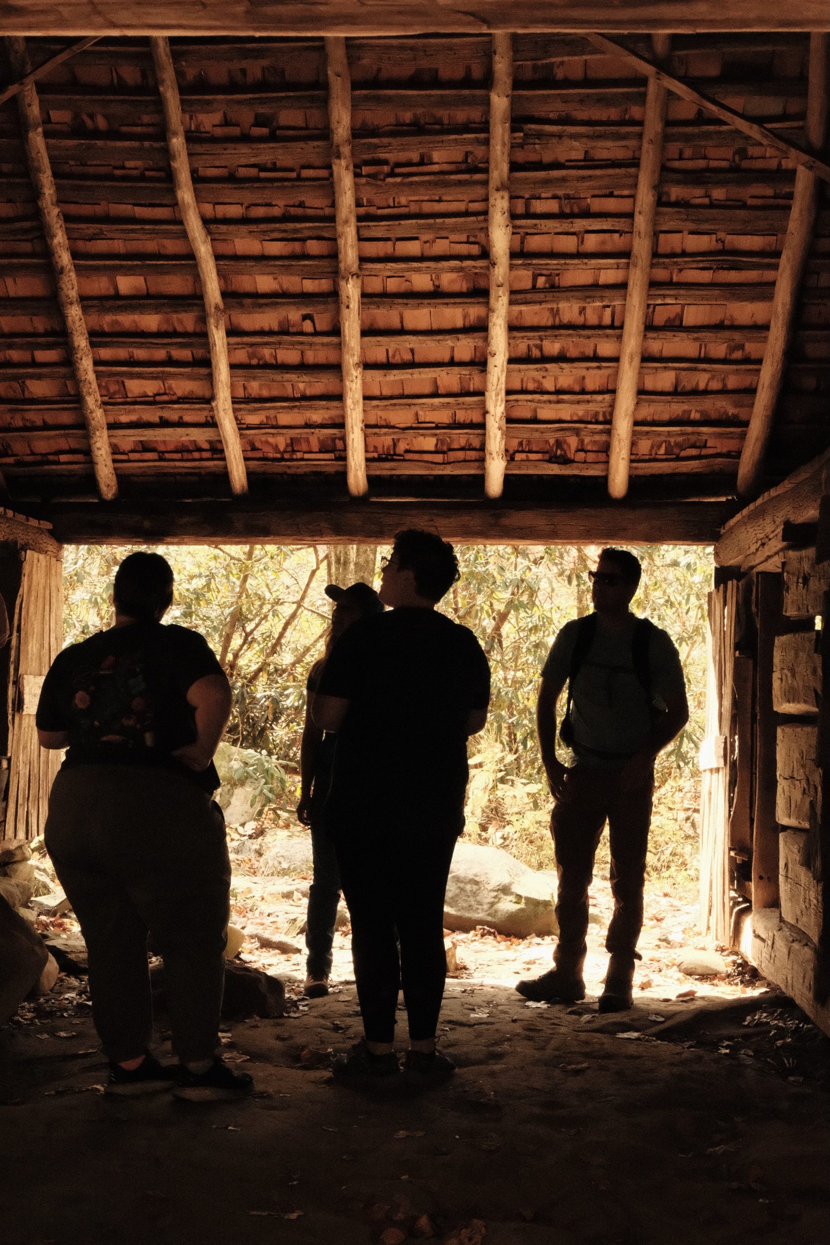 A group of people stand in silhouette inside an old barn.
