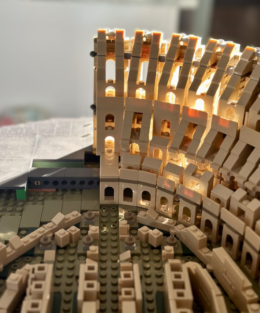 Golden hour sunlight hitting an unfinished LEGO model of the Colosseum from a top-down view.